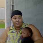 A Black woman holds her child while sitting on a porch
