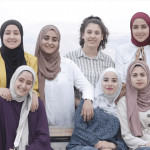 A group of young hijabi women pose for a photo, smiling at the camera
